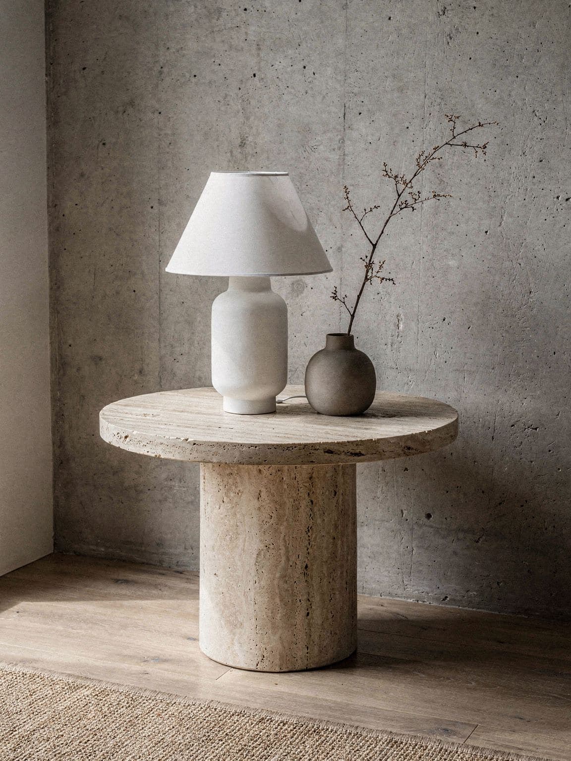 A chalk ceramic table lamp and a vase with a dried branch on a travertine side table