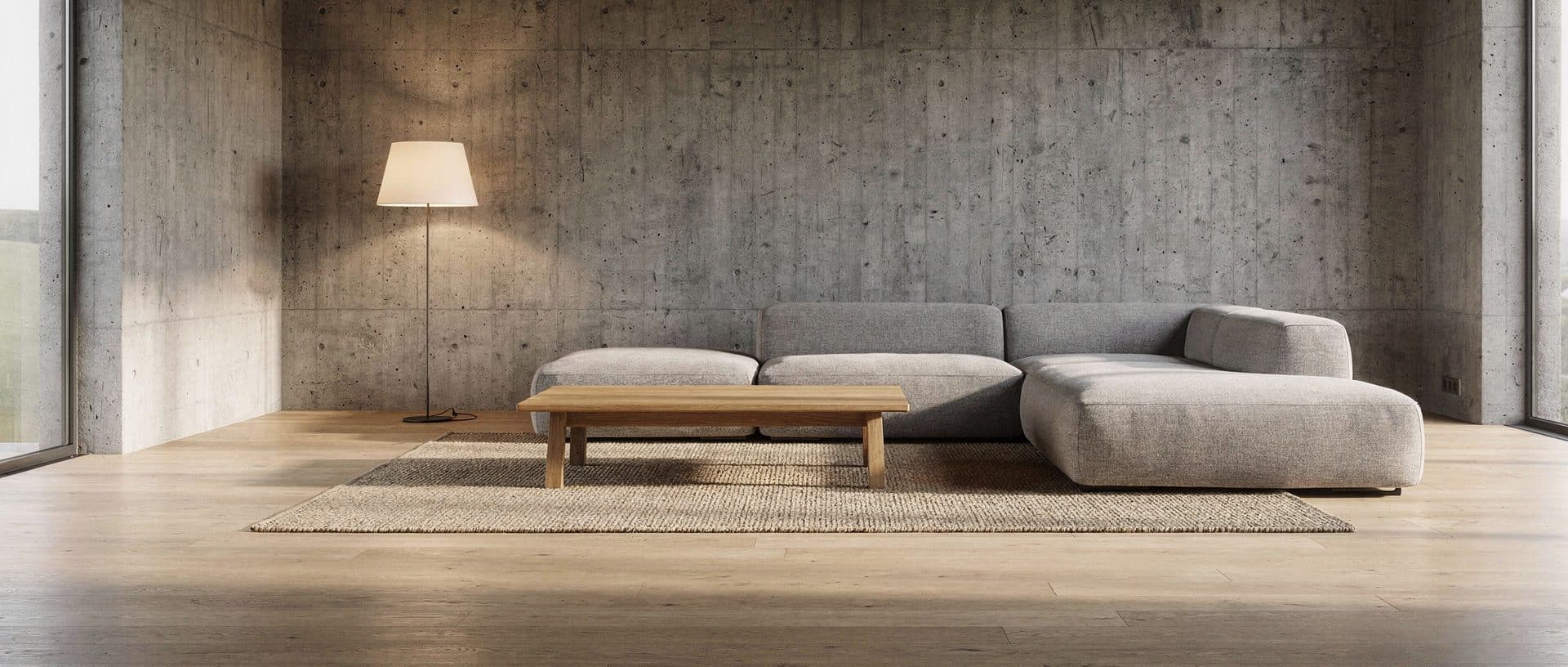 A long concrete-walled living room with a rounded grey corner sofa and an oak coffee table