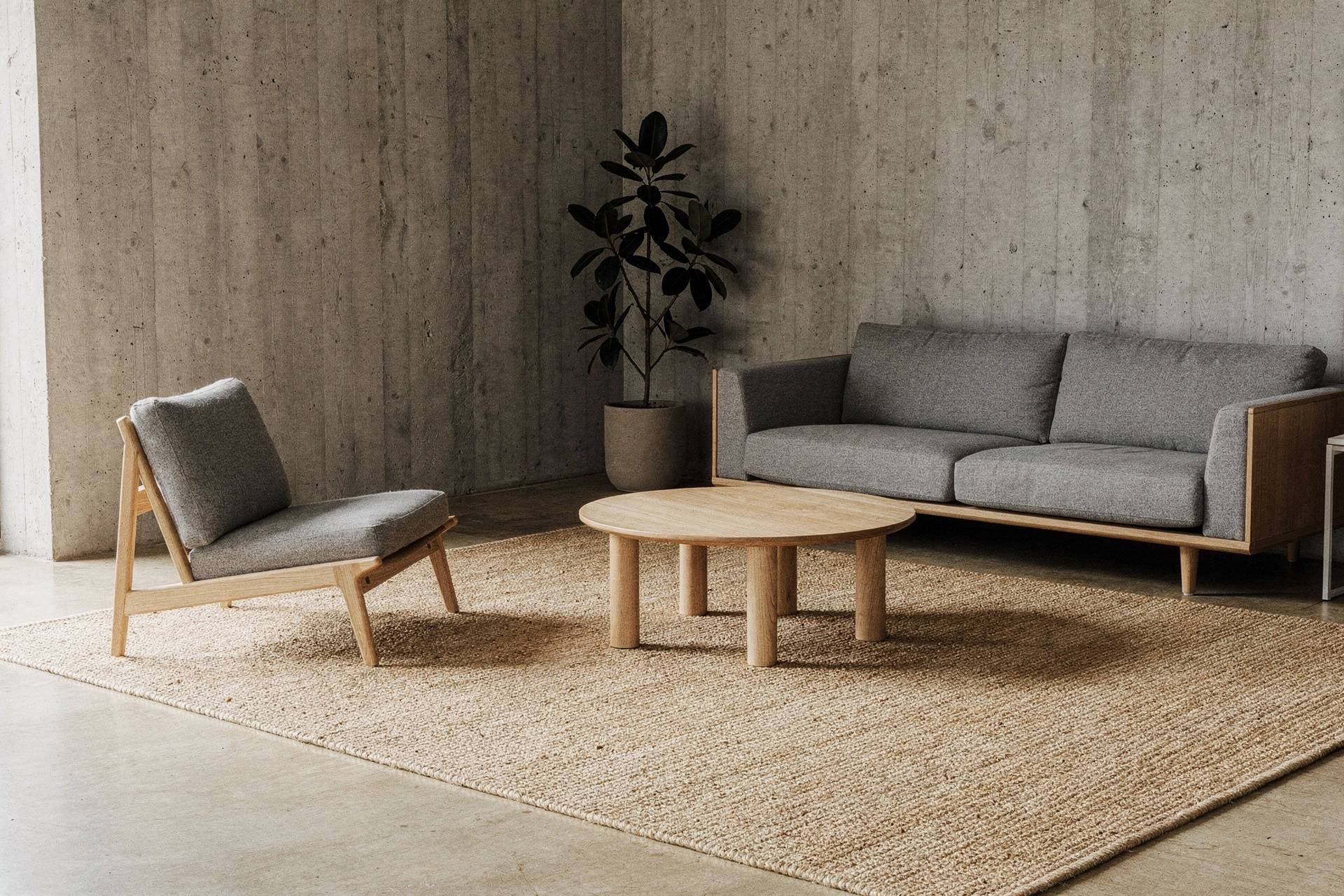 A grey sofa, an oak lounge chair and a round oak coffee table on a sisal rug in a concrete-walled living room